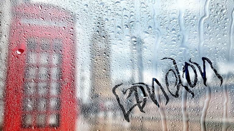 Una cabina roja de Londres y el Big Ben a través de una ventana mojada por la lluvia